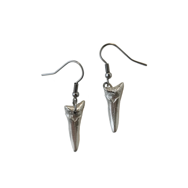 A pair of sterling silver earrings  sit on a white backdrop. These are shark tooth earrings. 